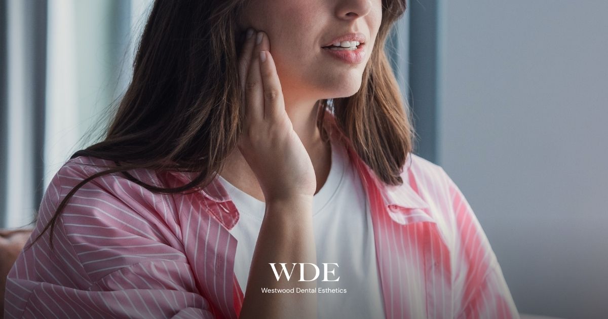  Person gently holding the side of their jaw, illustrating common temporomandibular disorder (TMD) symptoms such as jaw pain and facial discomfort.