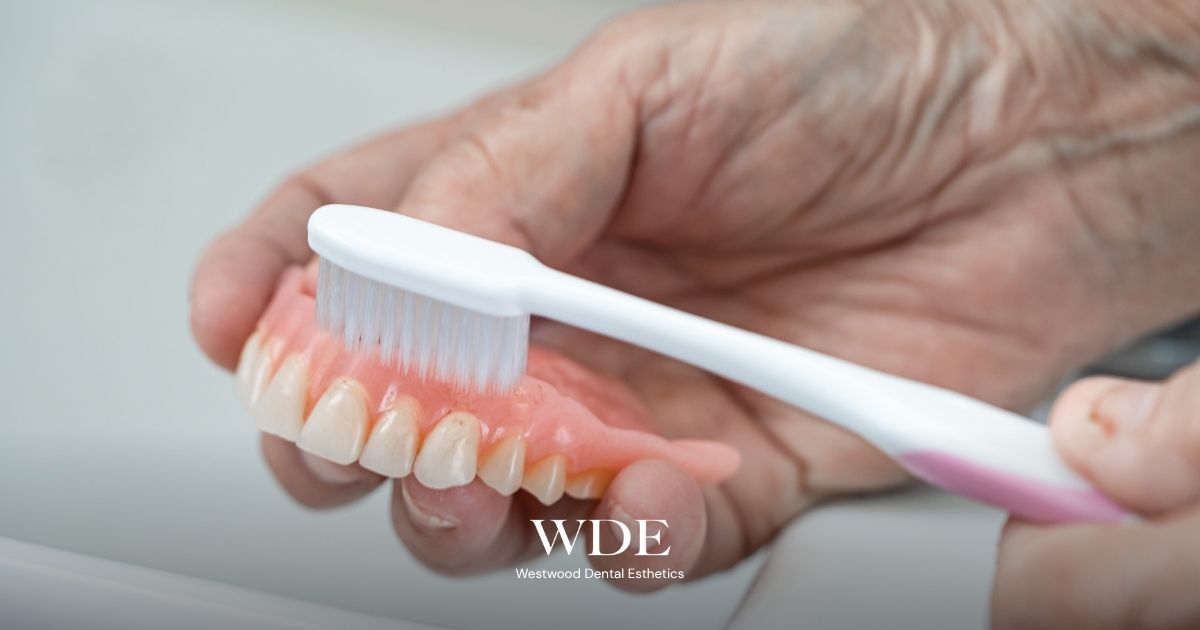 Hands brushing removable dentures to show cleaning techniques after receiving new dentures. 