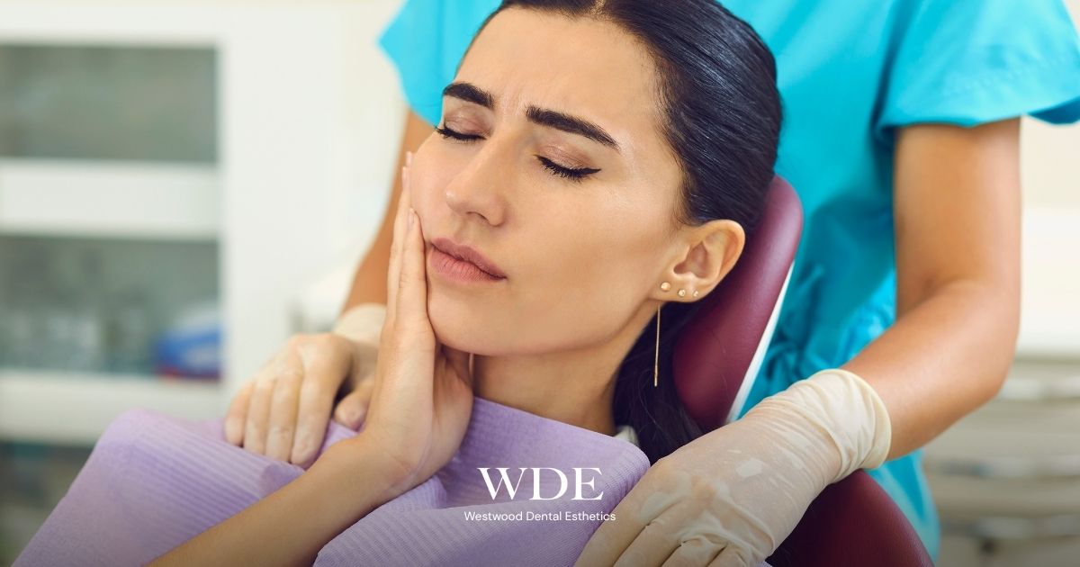 Patient holding their jaw while seated in a dental chair, illustrating increased pain that may occur several days after wisdom tooth extraction.